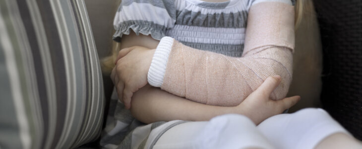 Little girl sitting on a couch holding her arm which has a cast on it