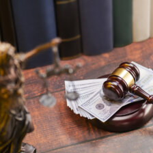 100 dollar bills on a gavel with lady justice statue in foreground